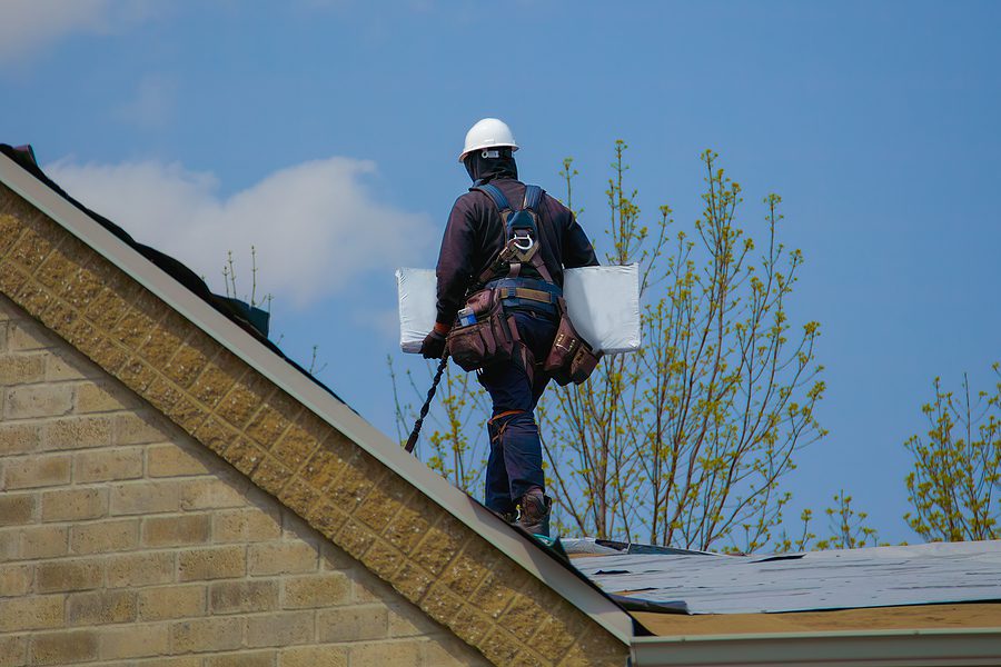 Professional roofer repairing a roof, carrying roofing supplies in arms.