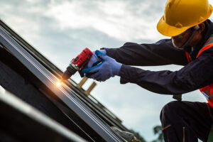 Professional roofer wearing protective gear and using an electric drill while installing a roof. 