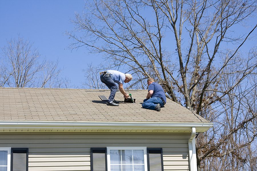 Roofing contractors repairing a roof that was damaged after a wind storm. 